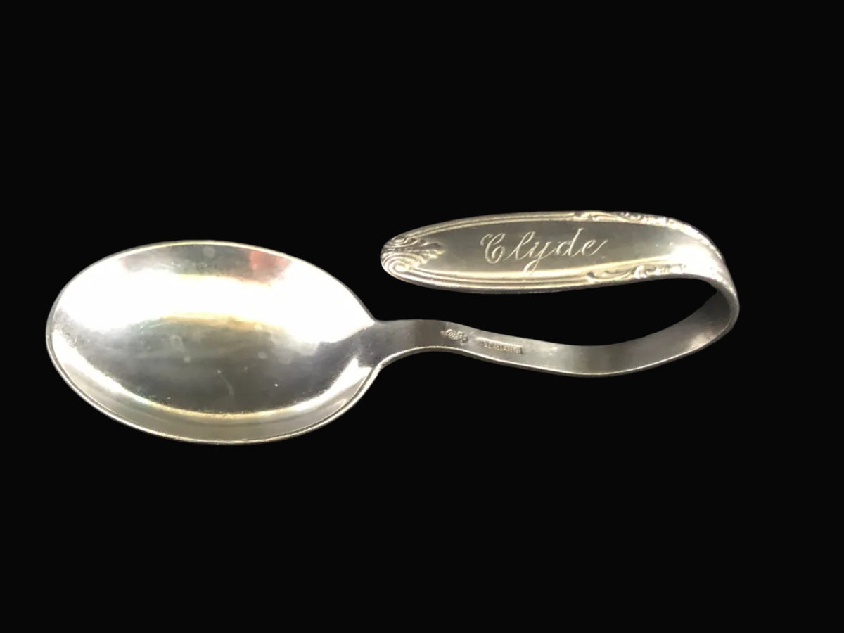 A vintage sterling silver spoon with a curved handle engraved with the name 'Clyde'.