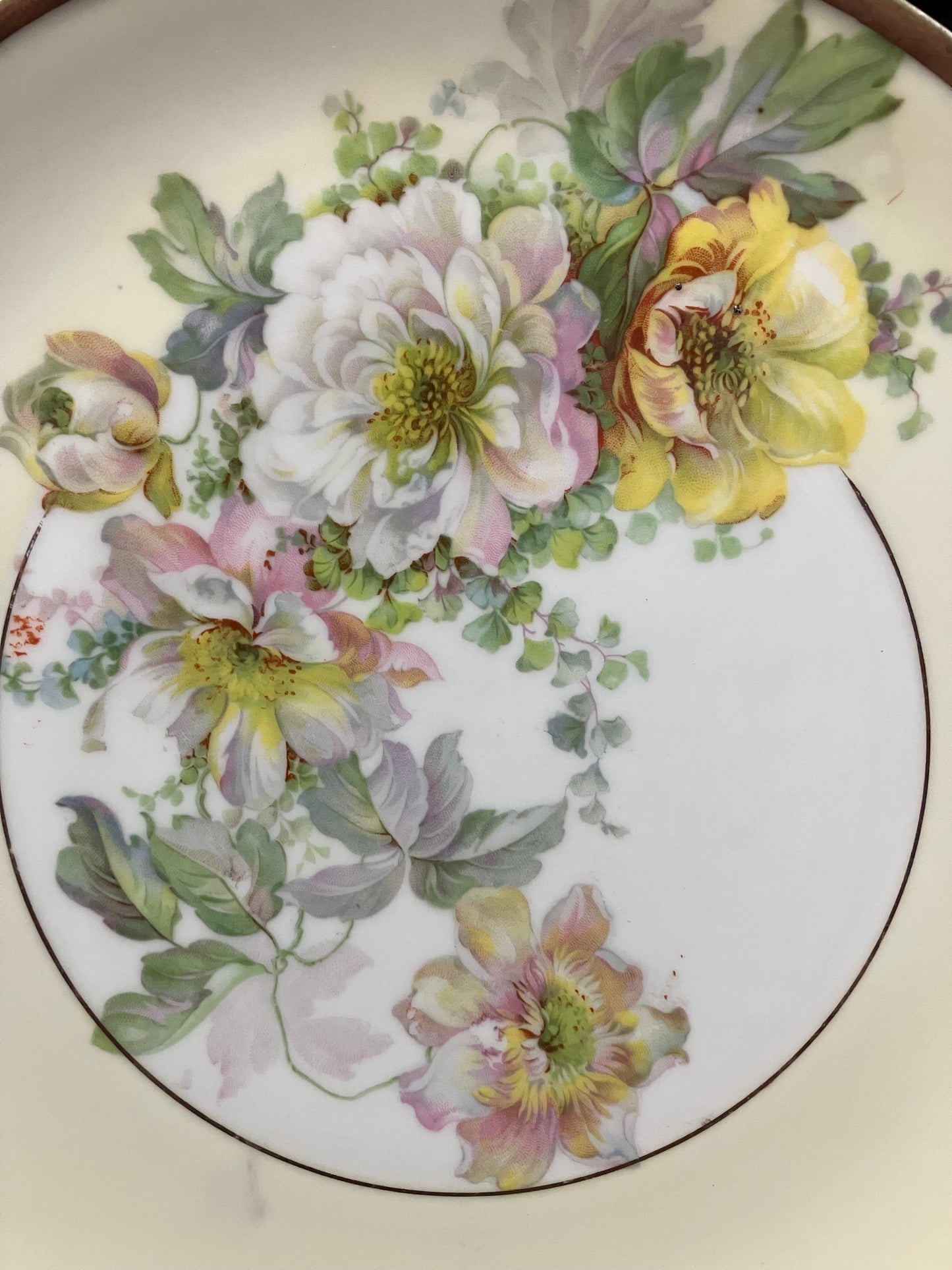 A close-up of a vintage ceramic plate or dish featuring a hand-painted floral design with white, yellow, pink, and green flowers on a white background.