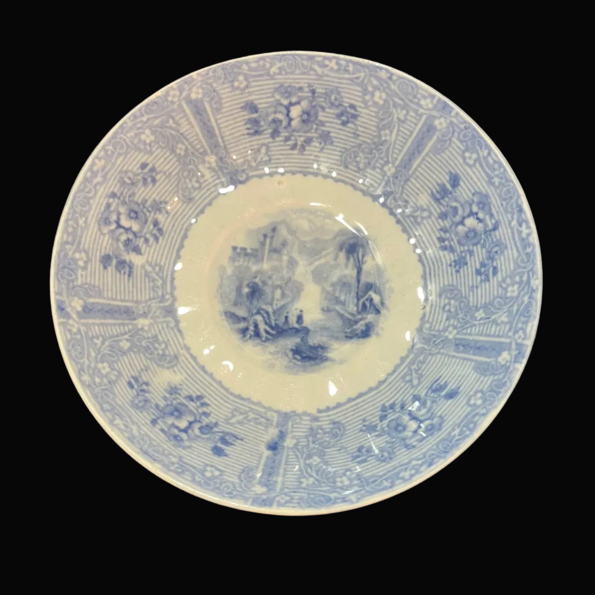 A round blue and white porcelain saucers with intricate floral and landscape illustrations, displayed on a draped black satin fabric background.