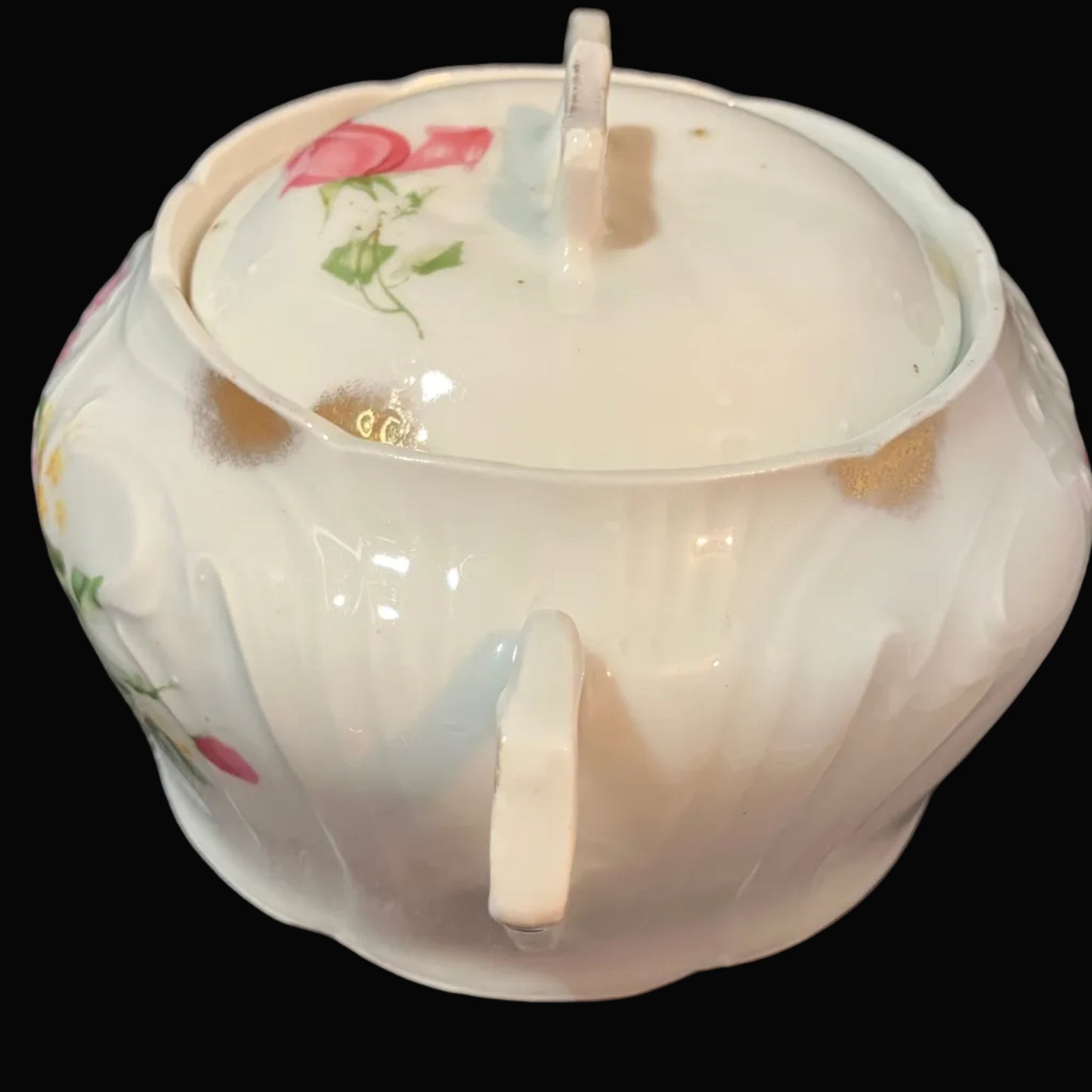 A white porcelain sugar bowl with a matching lid, decorated with pink roses and green leaves, set against a black background.