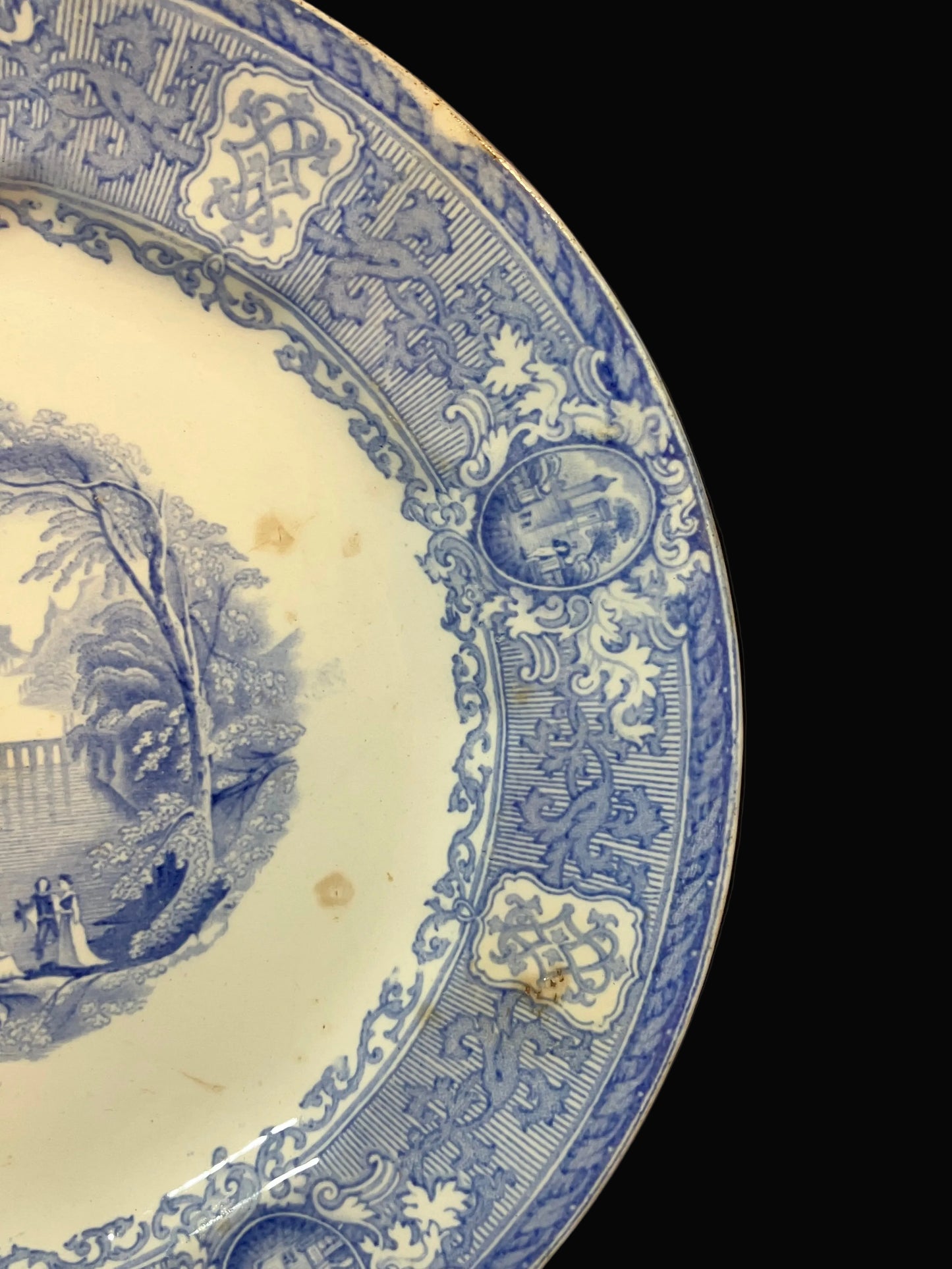 A close-up of a blue and white porcelain plate showing the decorative border and part of the landscape illustration on the inner side, photographed against a black background.