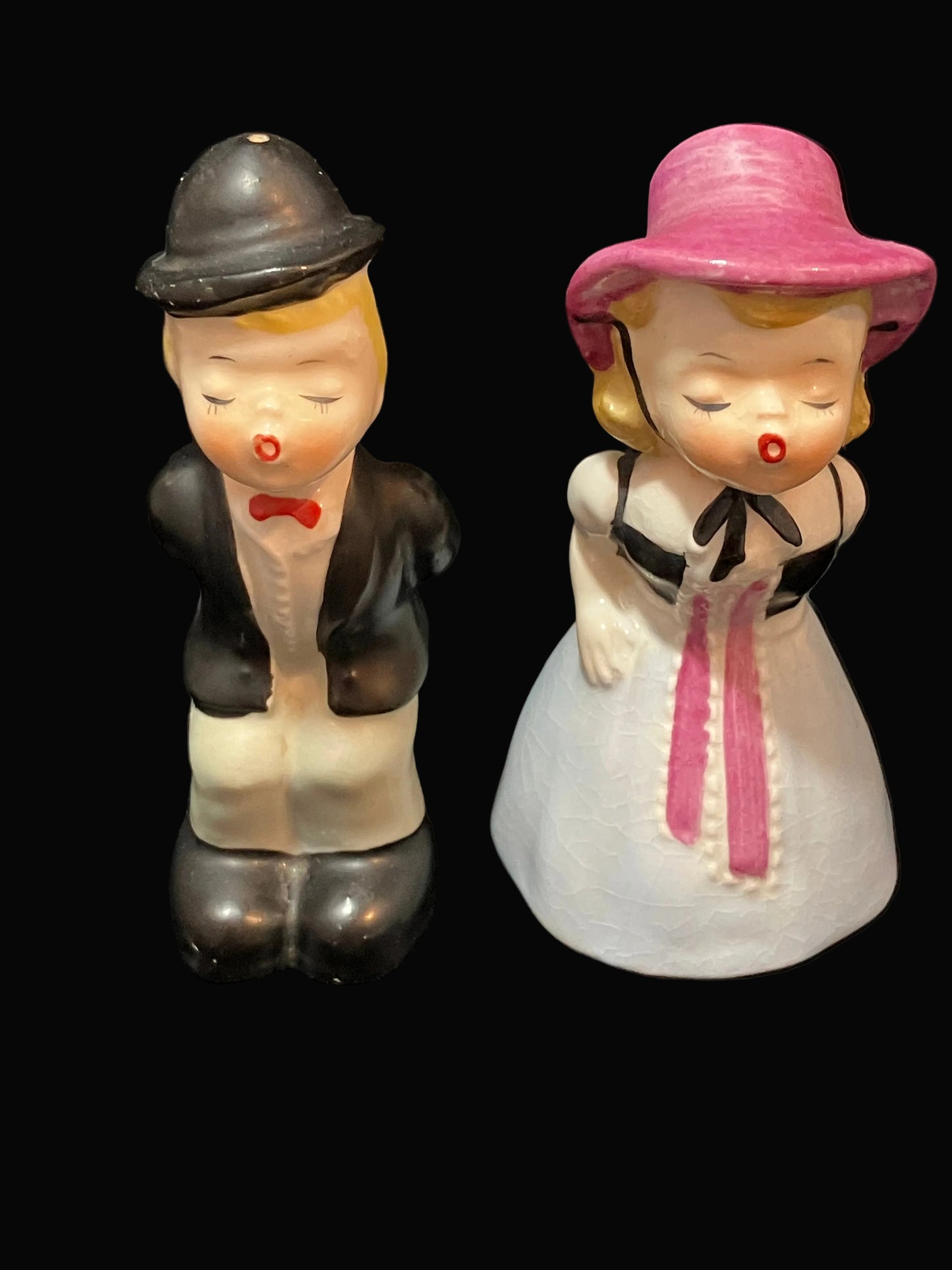 A pair of vintage ceramic salt and pepper shakers depicting a groom and bride. The groom figure wears a black bowler hat, black jacket, white pants, and a red bow tie.