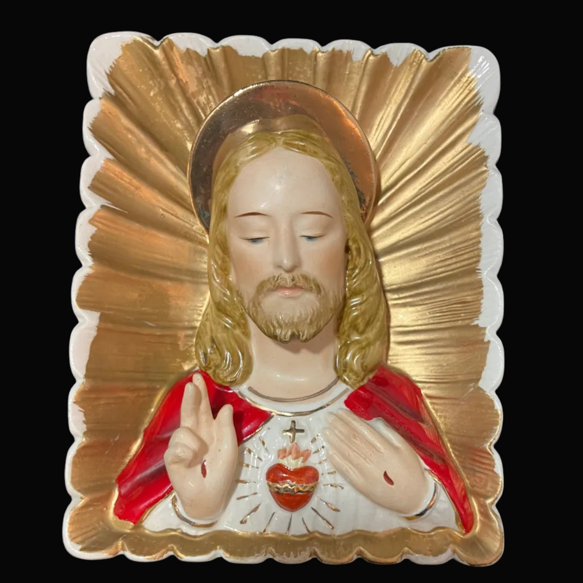 A religious figurine of the Sacred Heart of Jesus with a gold halo and red cape, set against a dark textured background.