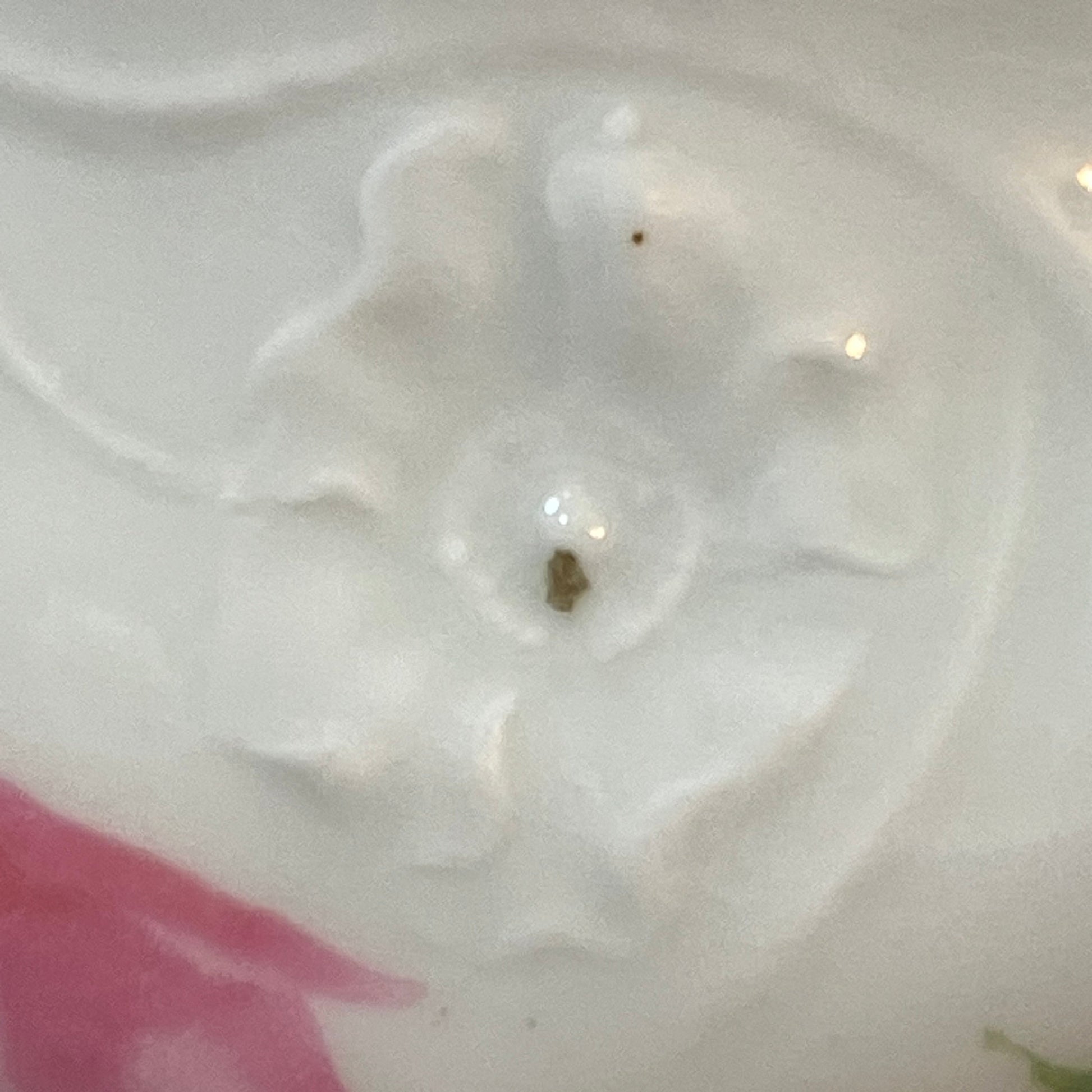 Close-up of a white ceramic surface with a floral embossed design and a pink and green painted floral motif at the bottom.
