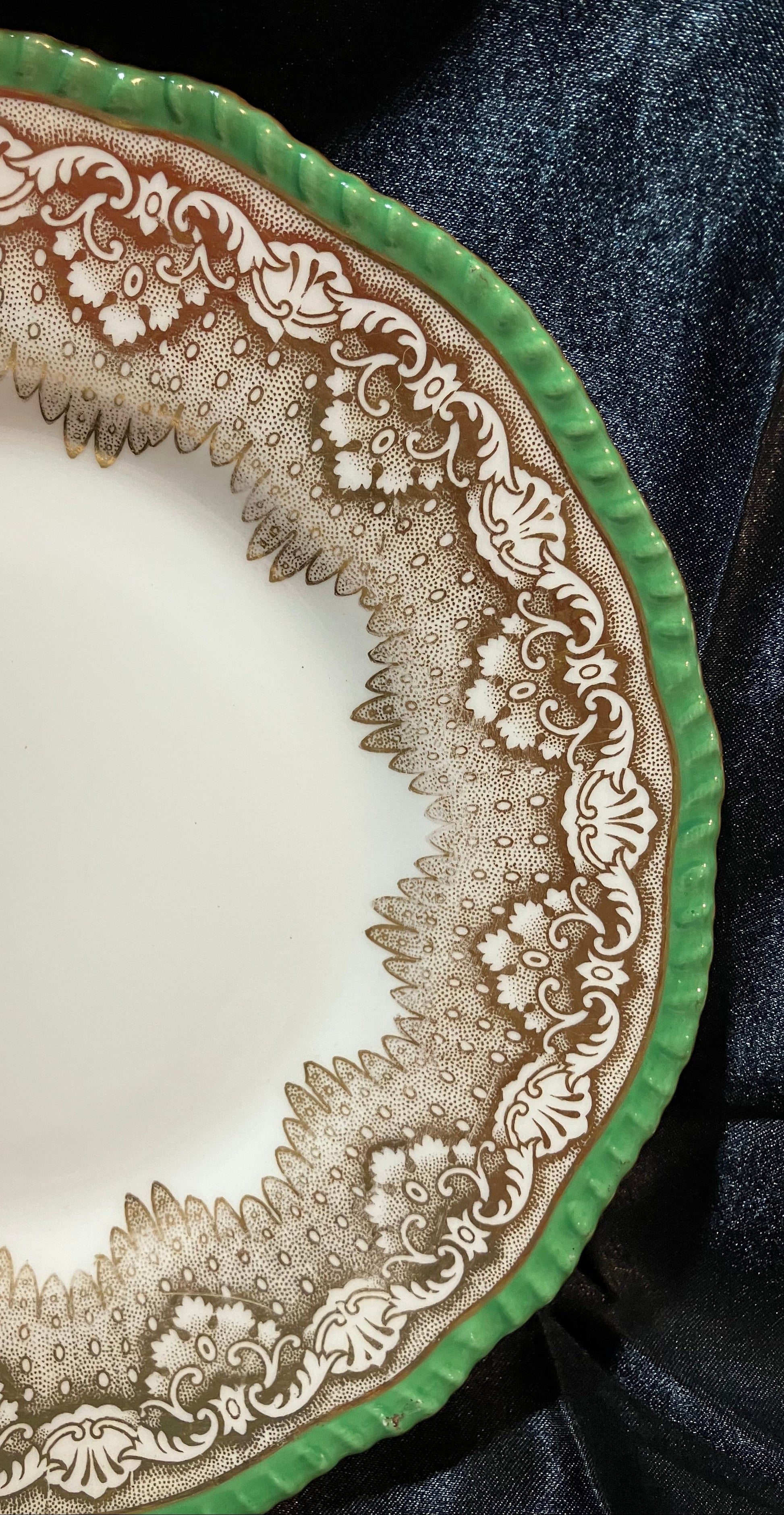Decorative plate with intricate brown patterns on a green rim, placed on a dark fabric surface.