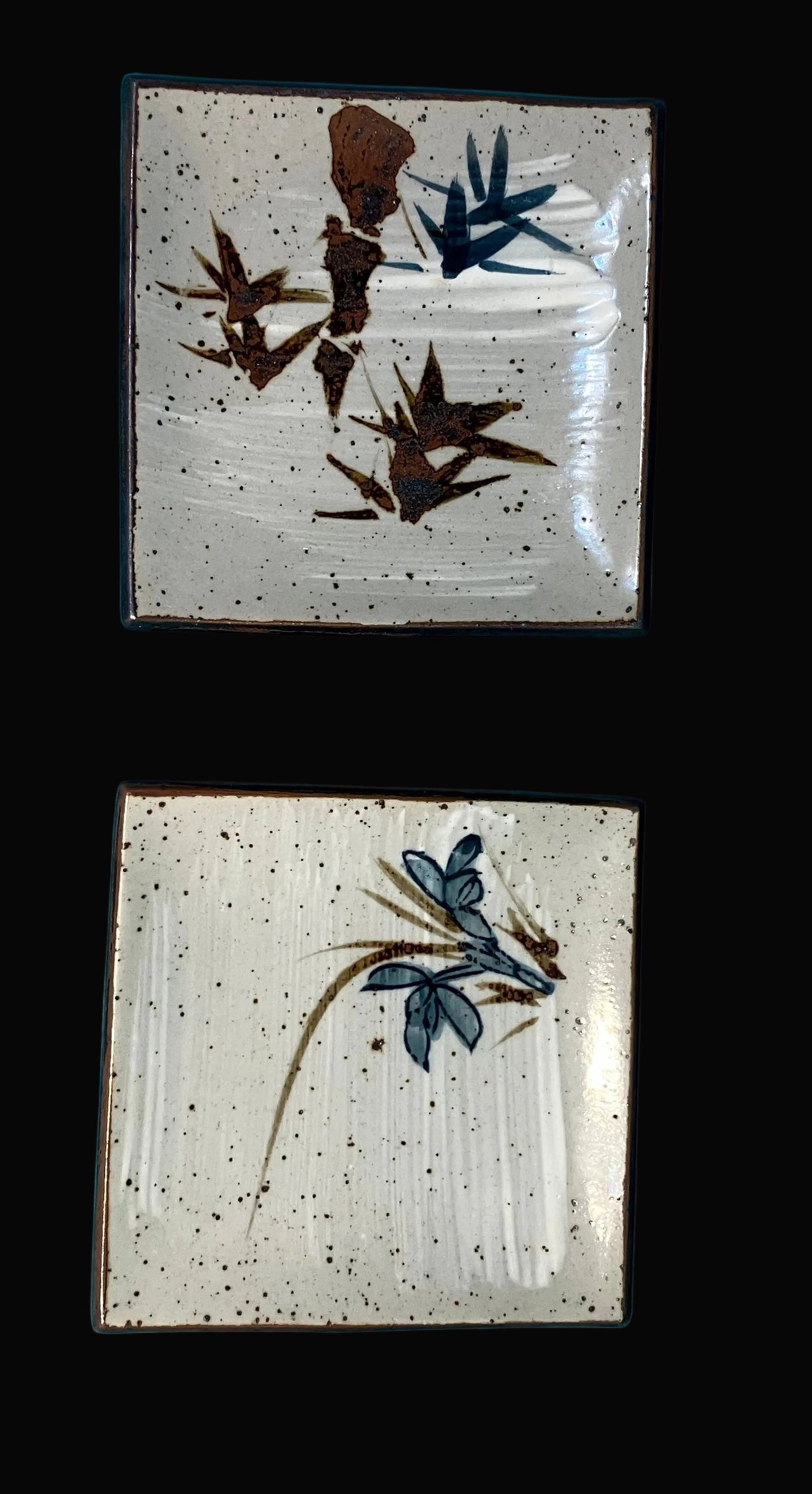 Two square ceramic plates with floral designs on a black background