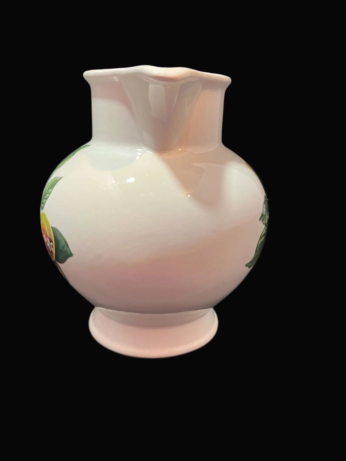 A glossy white ceramic pitcher with a flared neck and footed base, decorated with green leaves and small yellow/orange fruit motifs.