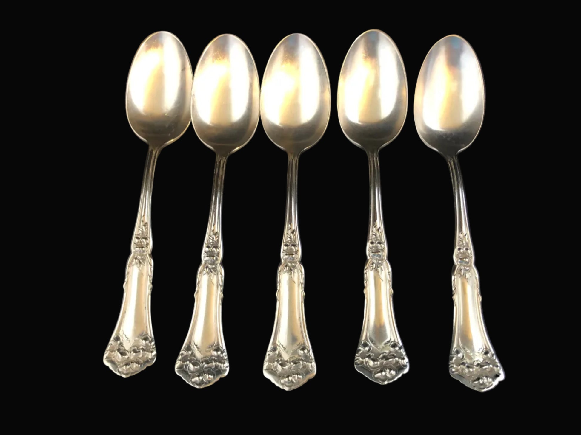 Set of five silverplate spoons with decorative handles on a black background