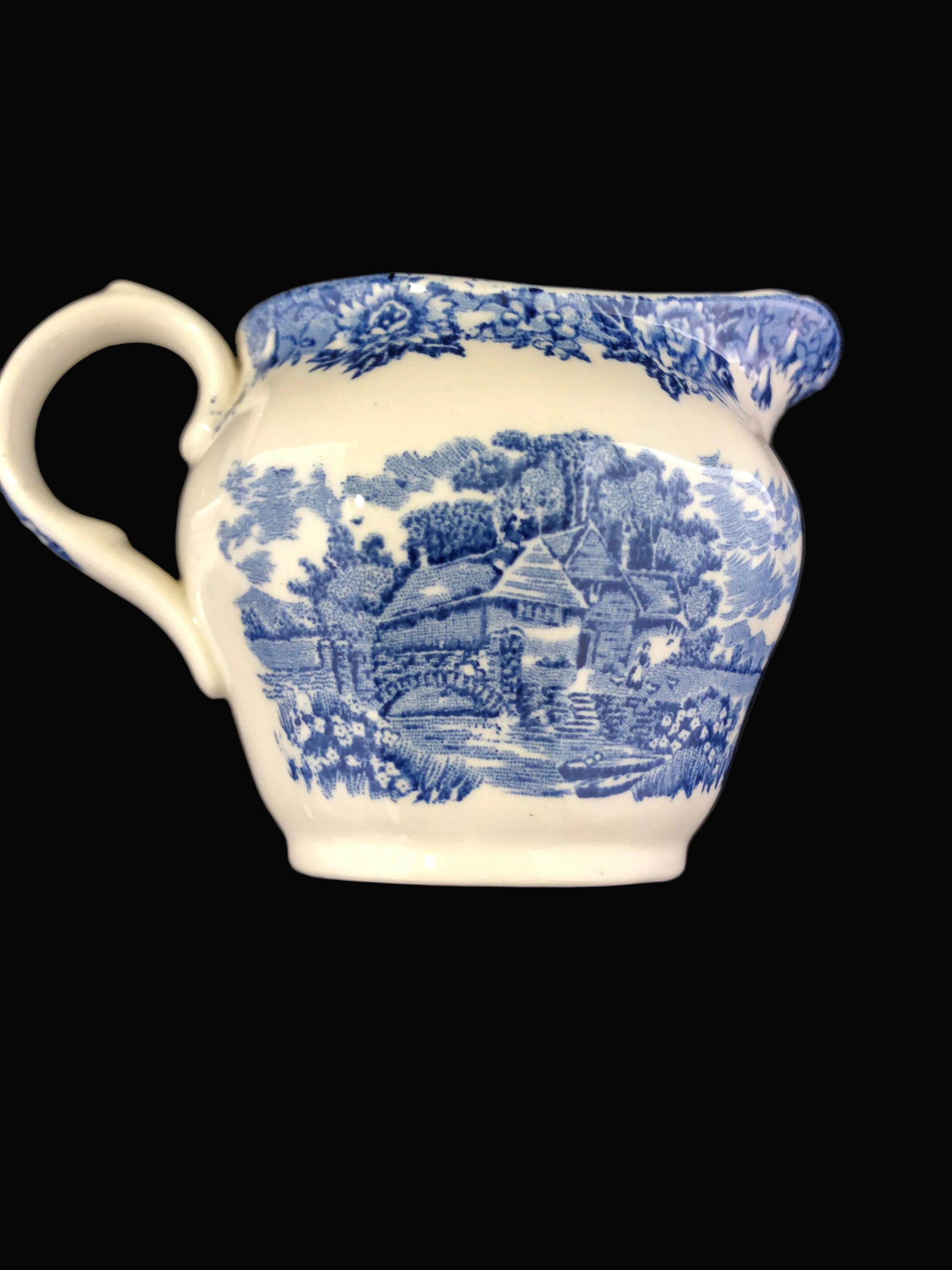 A vintage ceramic creamer with a blue and white transfer landscape design by Salam China, set against a dark  background.