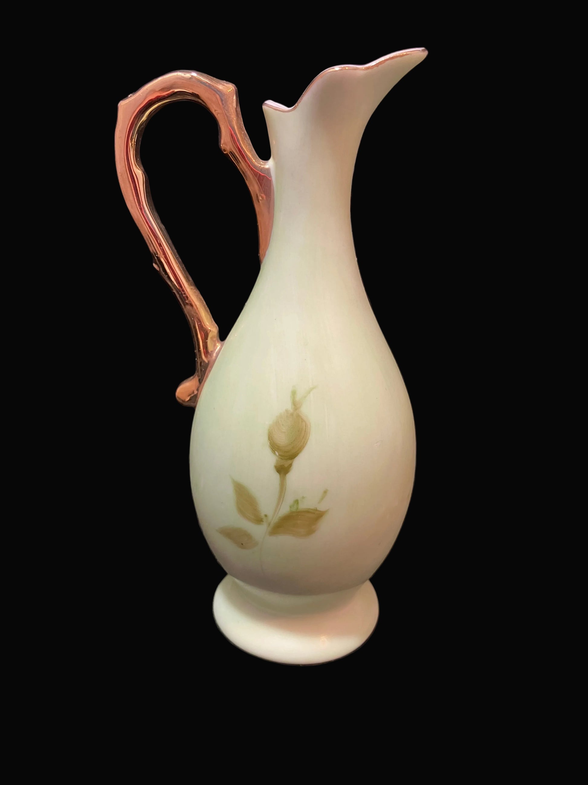 A vintage Mid Century Lefton 5 inch green  ceramic pitcher with a rose gold metallic handle and base, decorated with a gold rose bud and leaf motif on the front, set against a solid black background.
