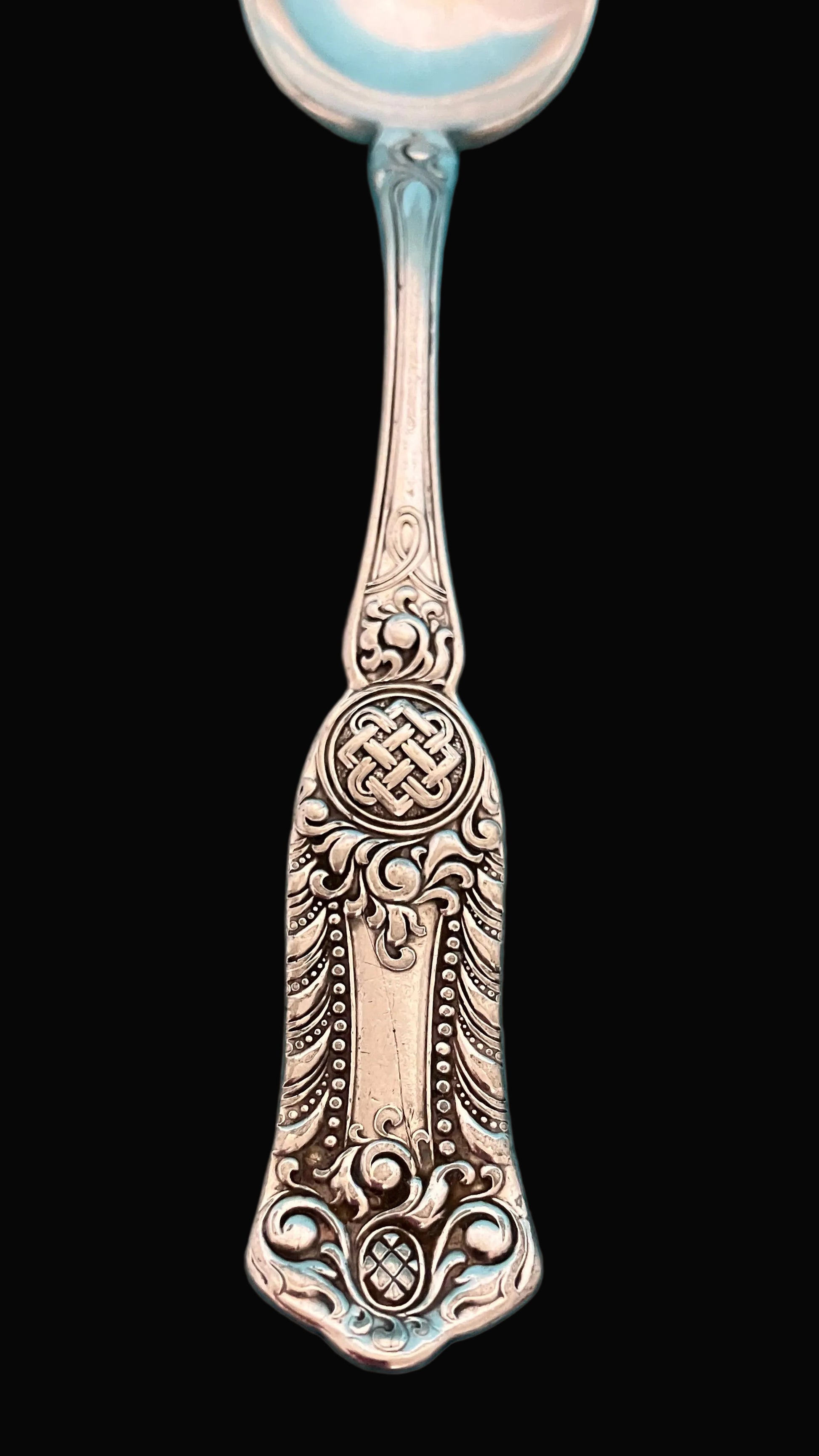 Decorative silver spoon with intricate patterns on a black background