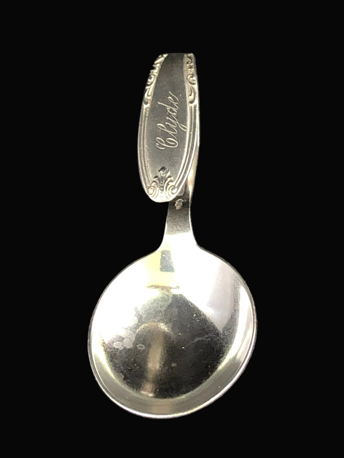 A vintage silver spoon with an engraved handle featuring the name 'Cylde' and decorative scrollwork, background.