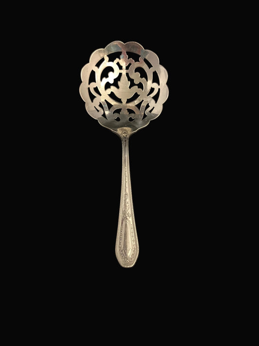 An ornate vintage silver-toned metal serving spoon or ladle with a decorative cutout pattern on the bowl and an engraved handle, shown against a solid black background.
