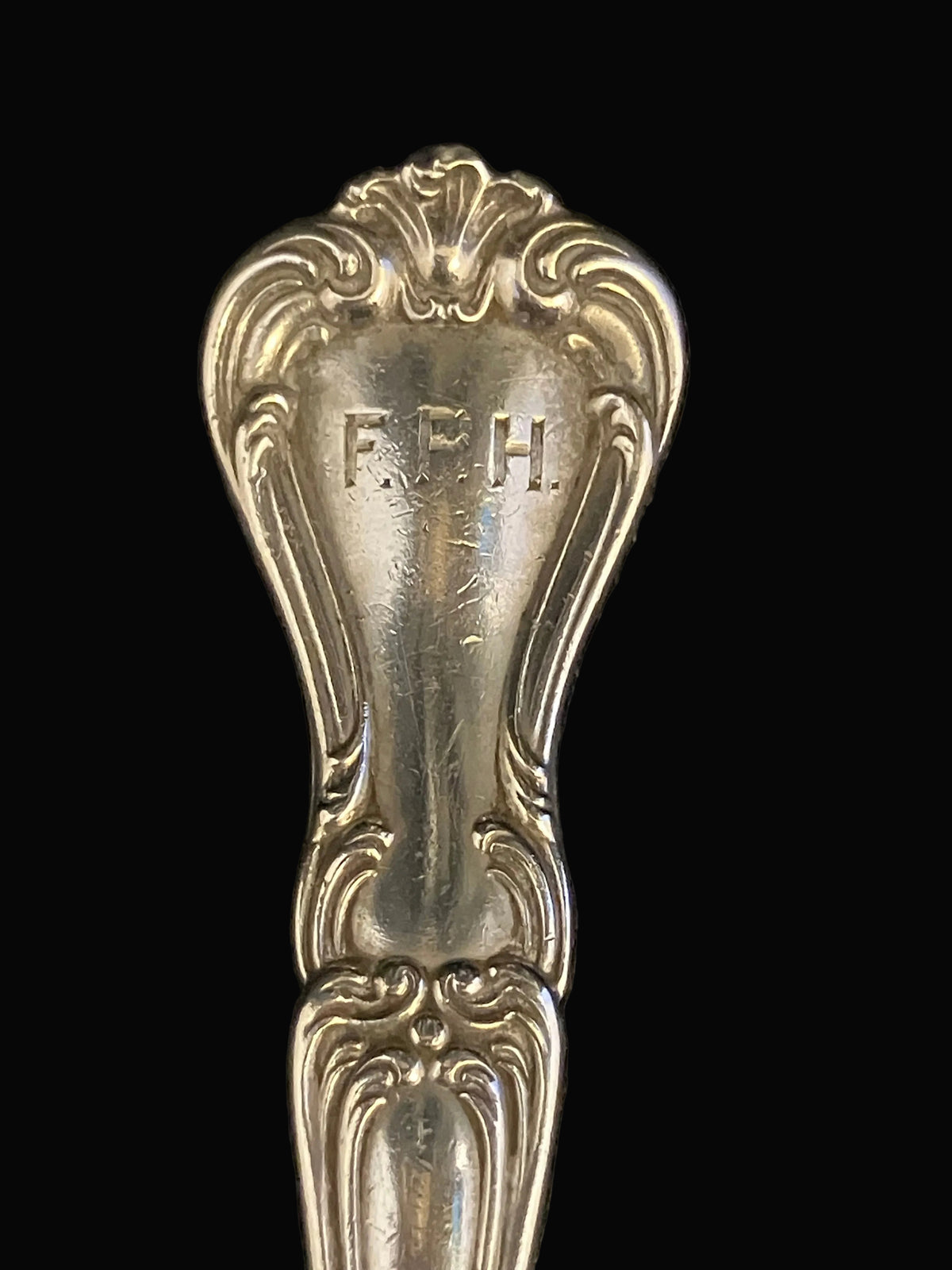 An ornate vintage sterling silver spoon handle with engraved initials FRH
