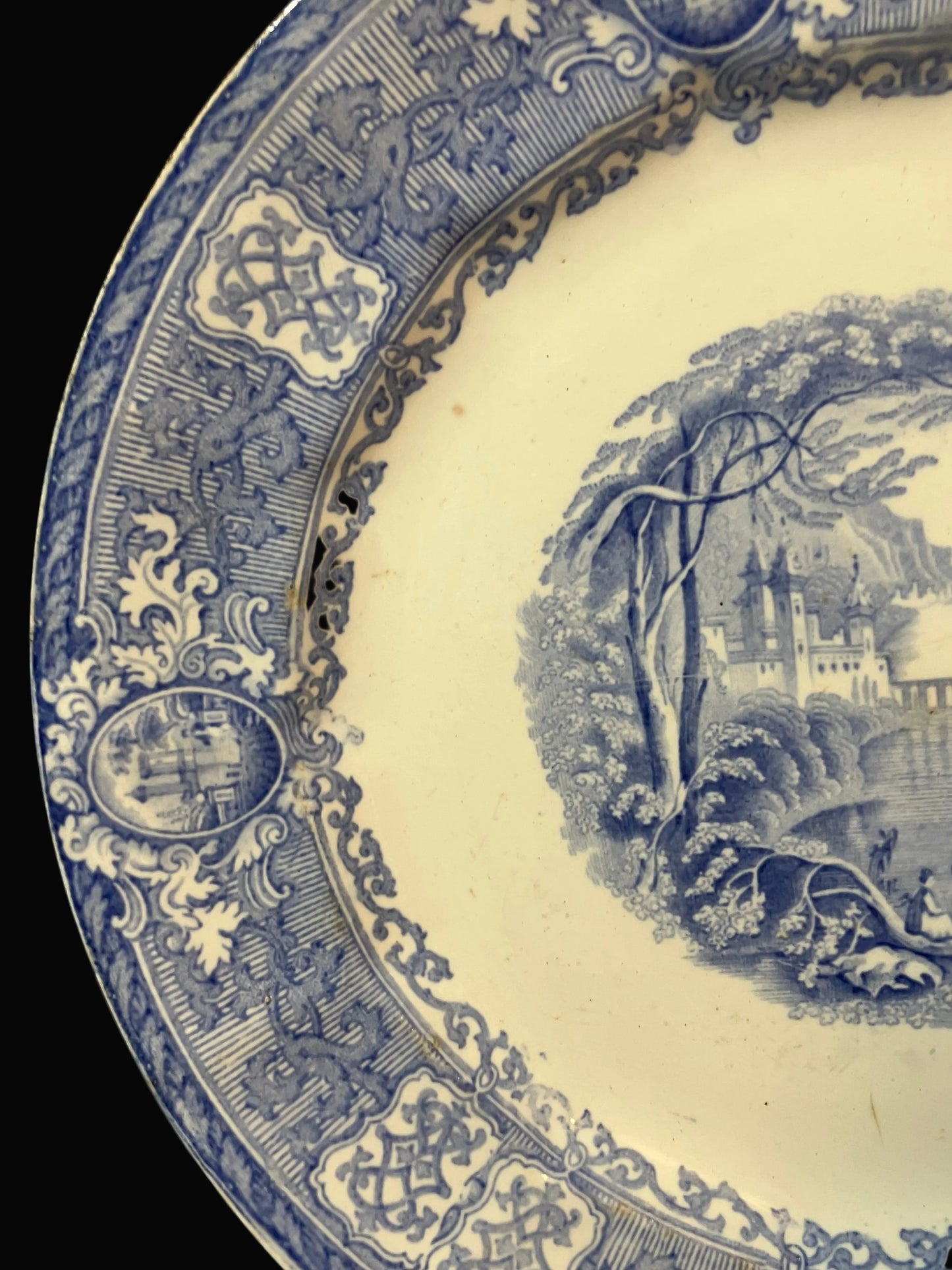 Close-up of a blue and cream ceramic plate showing the decorative border and part of the landscape transfer design.