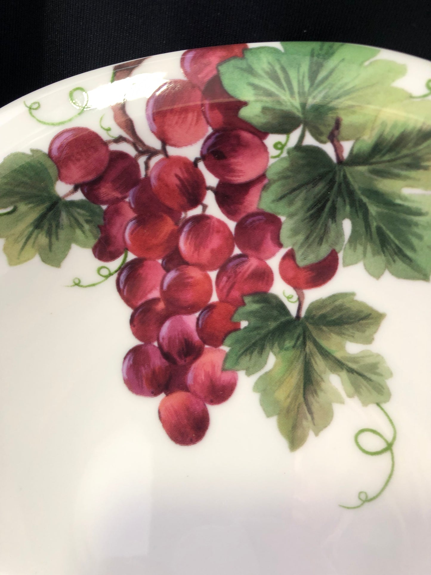 Decorative plate with a painting of red grapes and green leaves on a white background