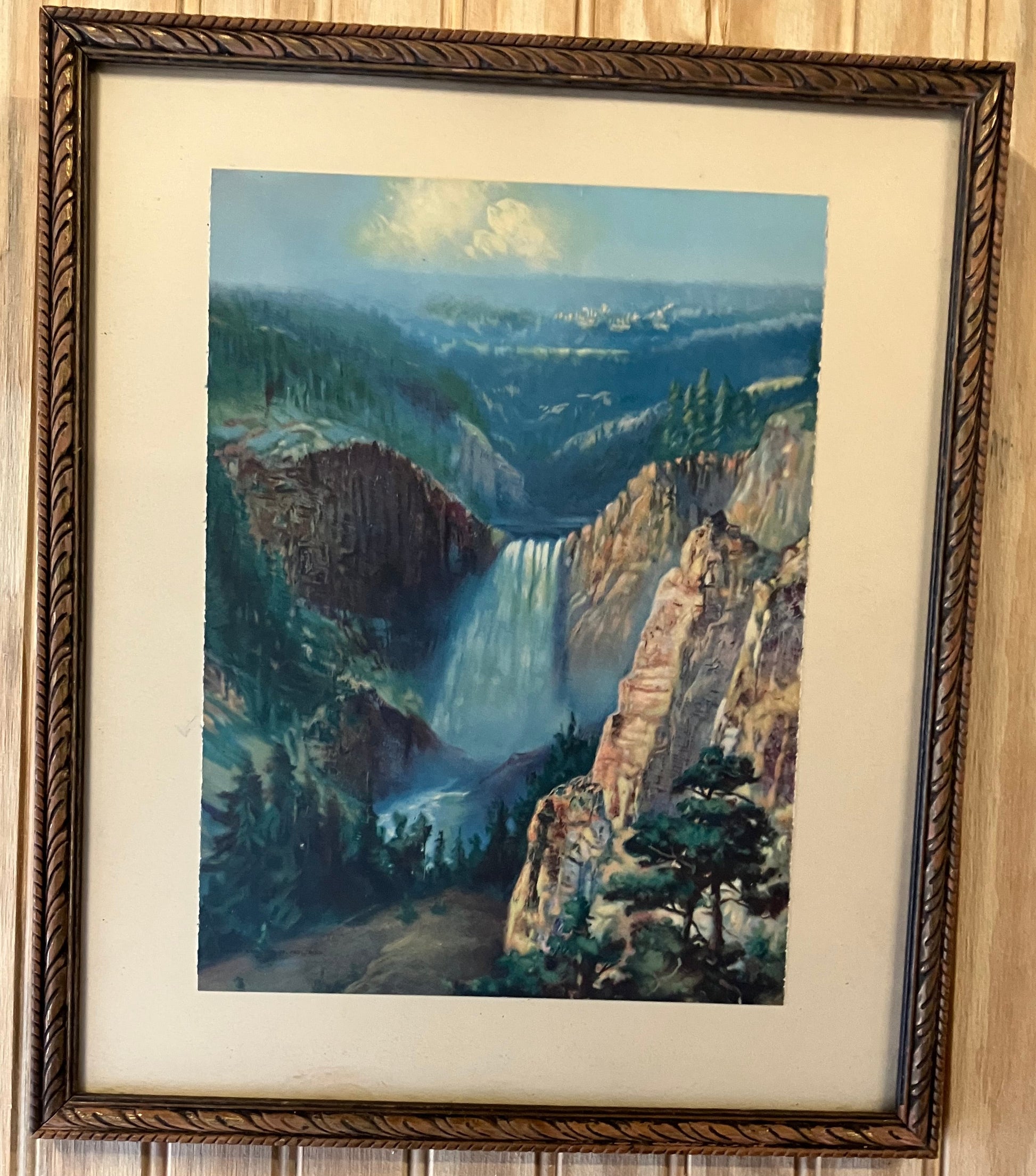Framed artwork of a landscape with a body of water on a wooden wall.