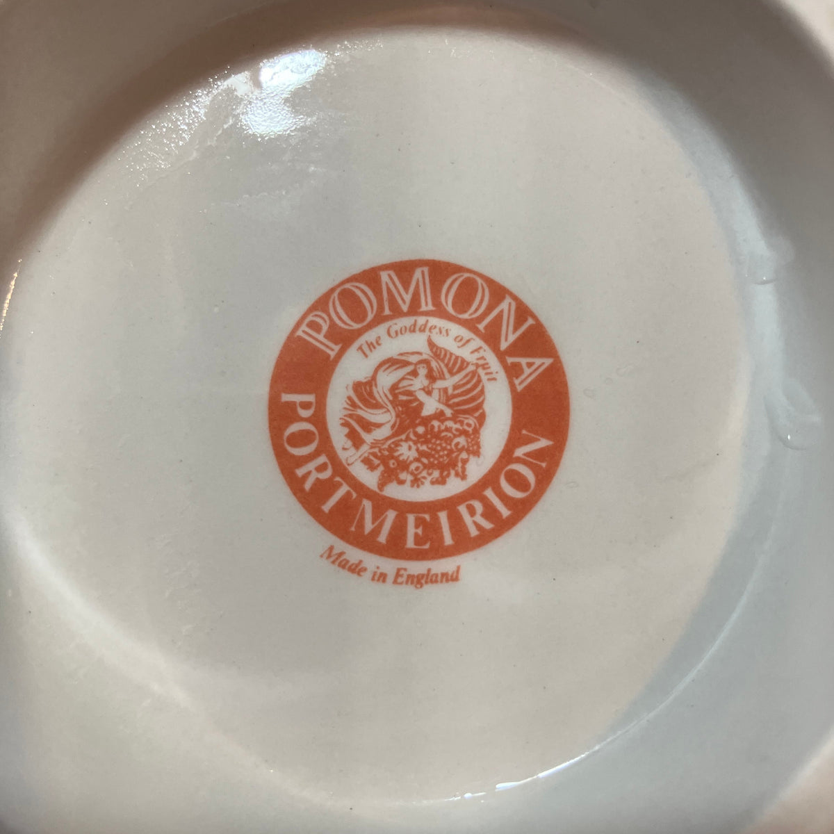 The bottom of a white ceramic dish or plate featuring a circular orange-red printed logo that reads 'POMONA PORT MEIRION'  and 'Made in England' below.