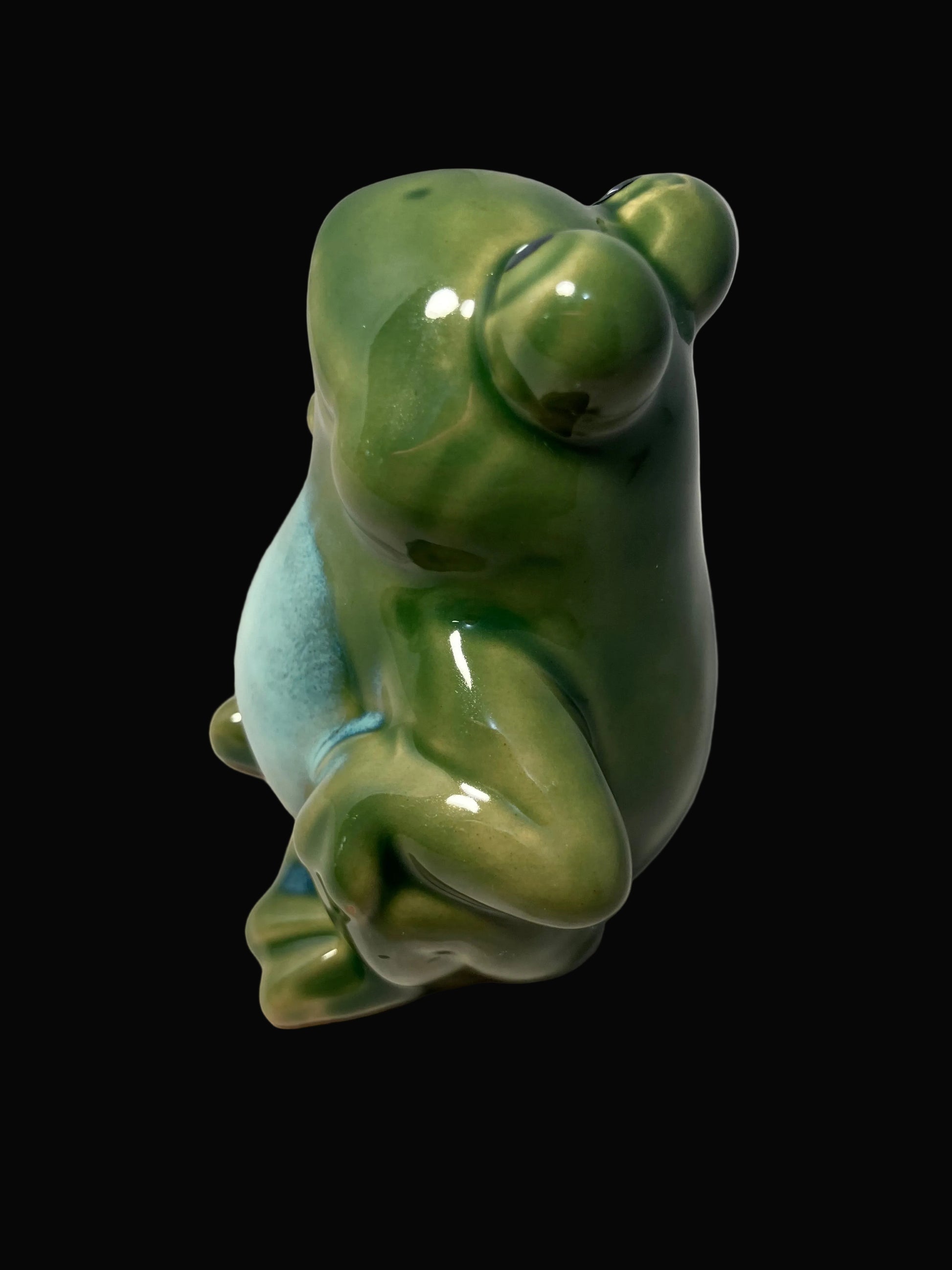 Green ceramic frog figurine on a black background