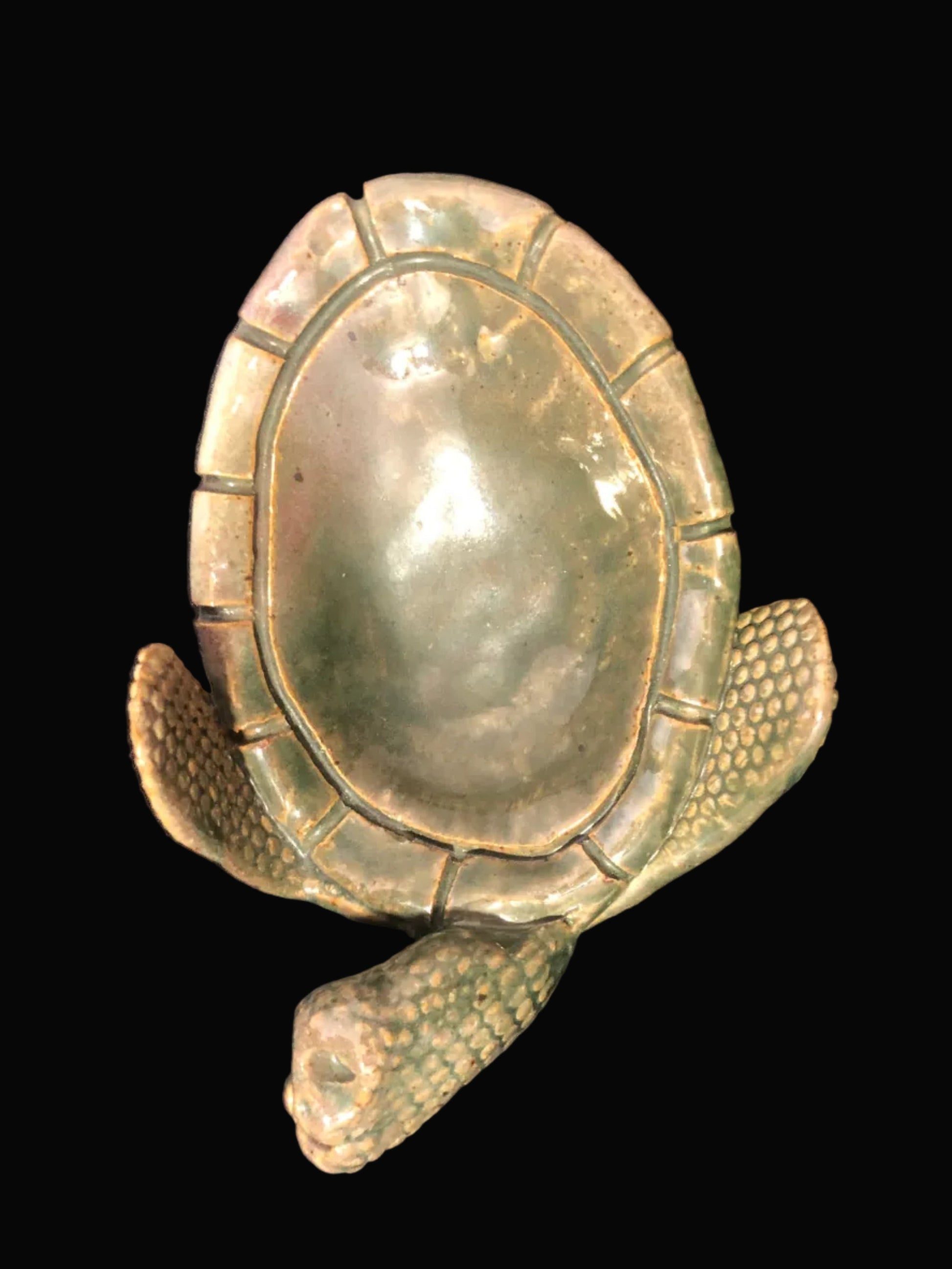 A pottery turtle-shaped dish with a textured, weathered green and brown finish, set against a black background.