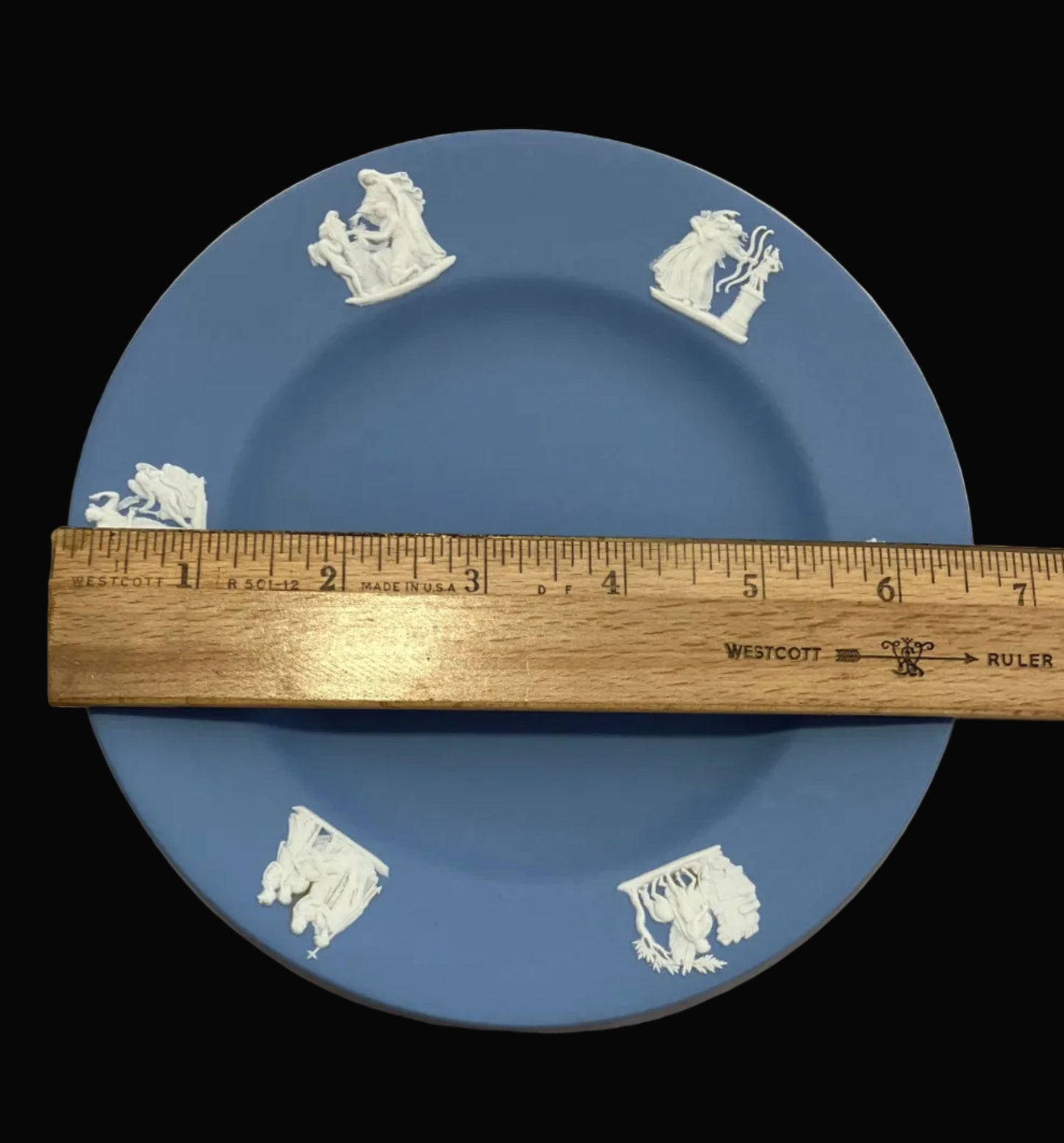 Blue plate with white patterns and a wooden ruler for scale on a beige background