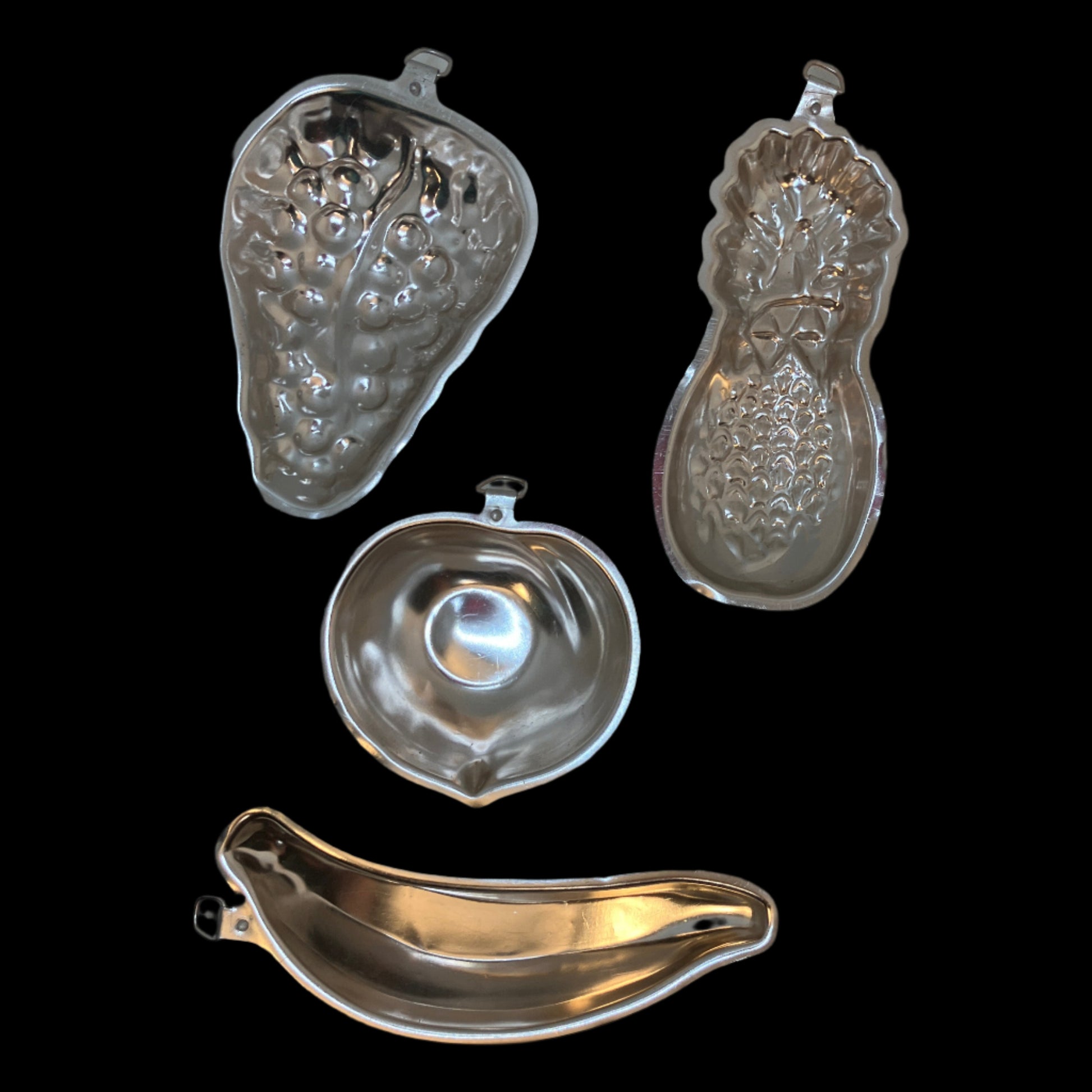 A set of 4 vintage aluminum jello molds, each featuring a classic fruit shape: banana, peach, pineapple, and grape