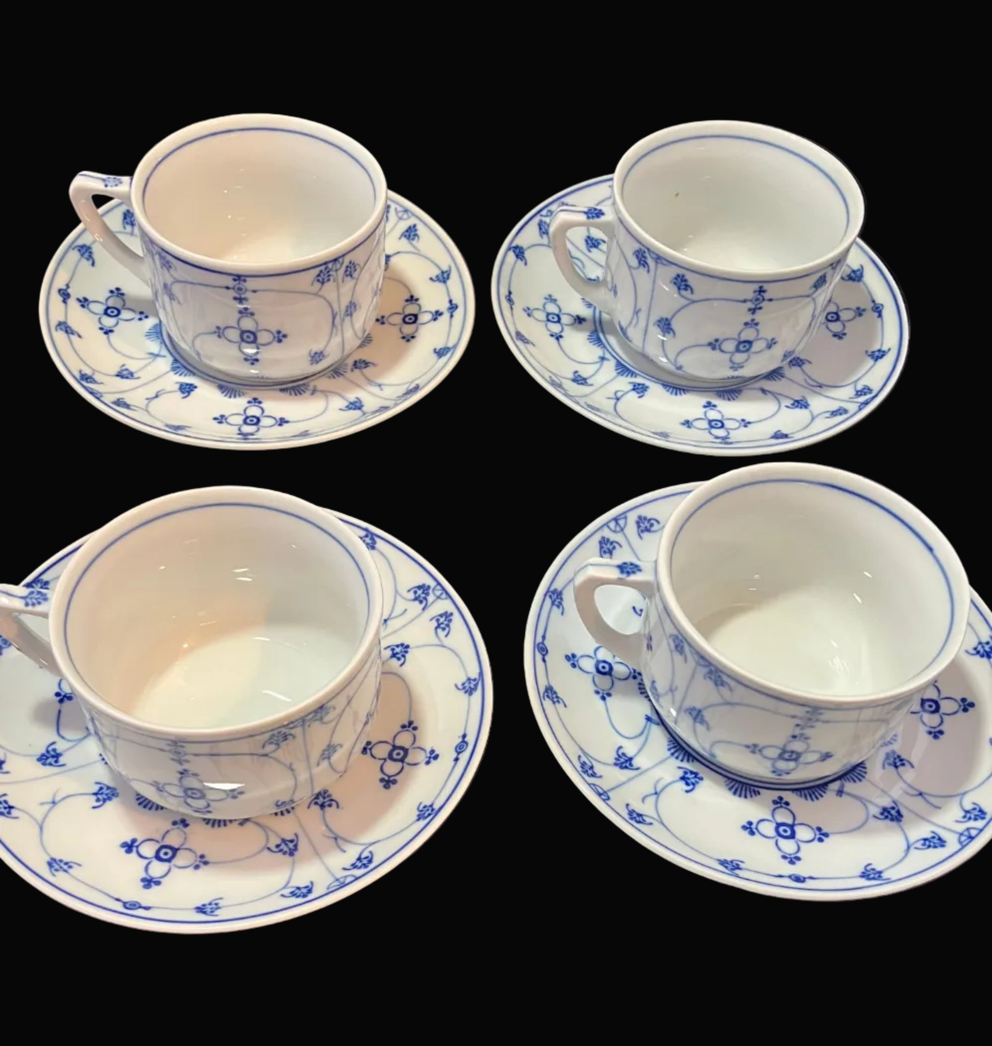 Set of four white teacups with blue floral patterns on a black surface