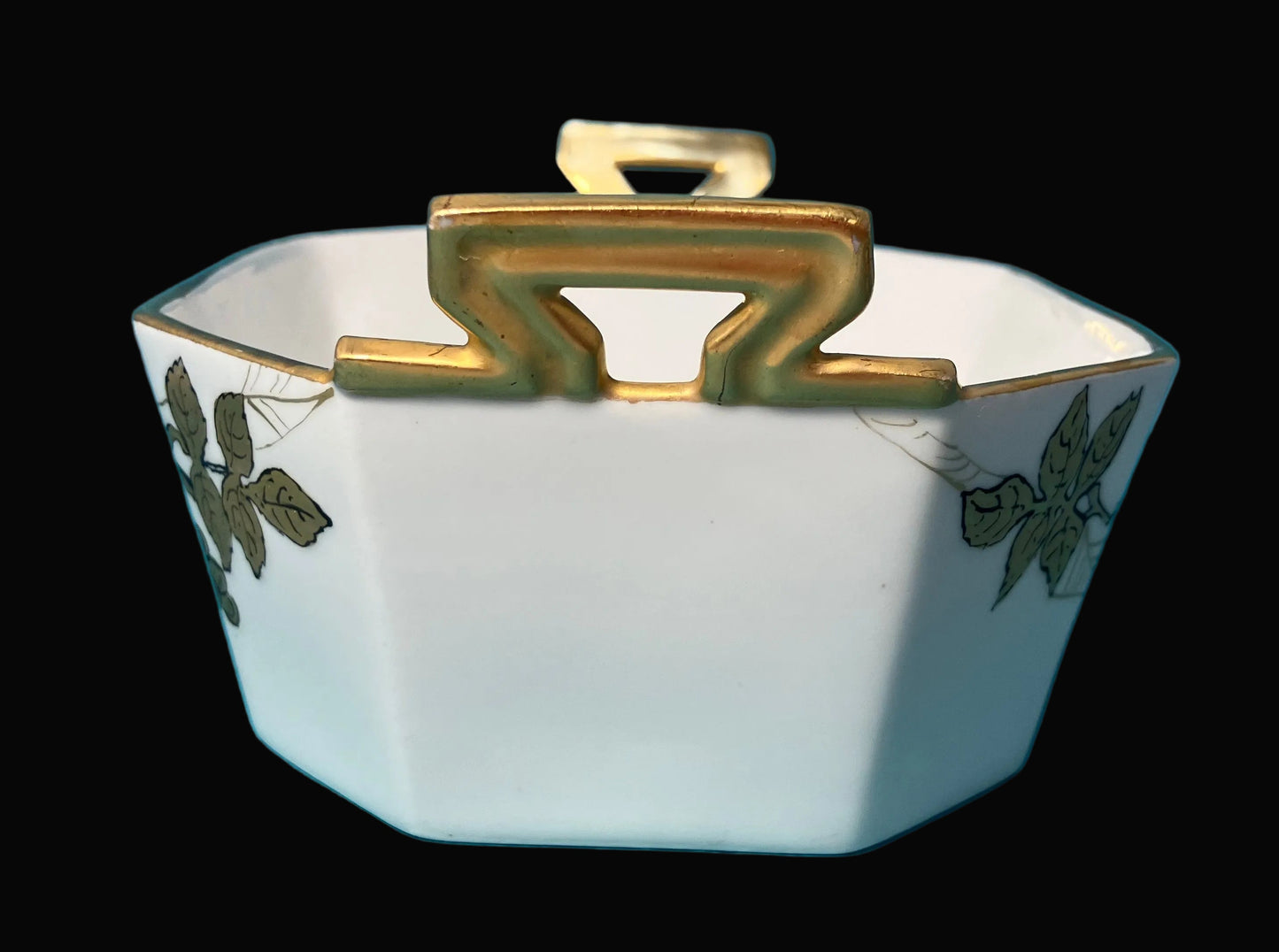 Decorative ceramic bowl with gold accents and green leaf patterns on a black background