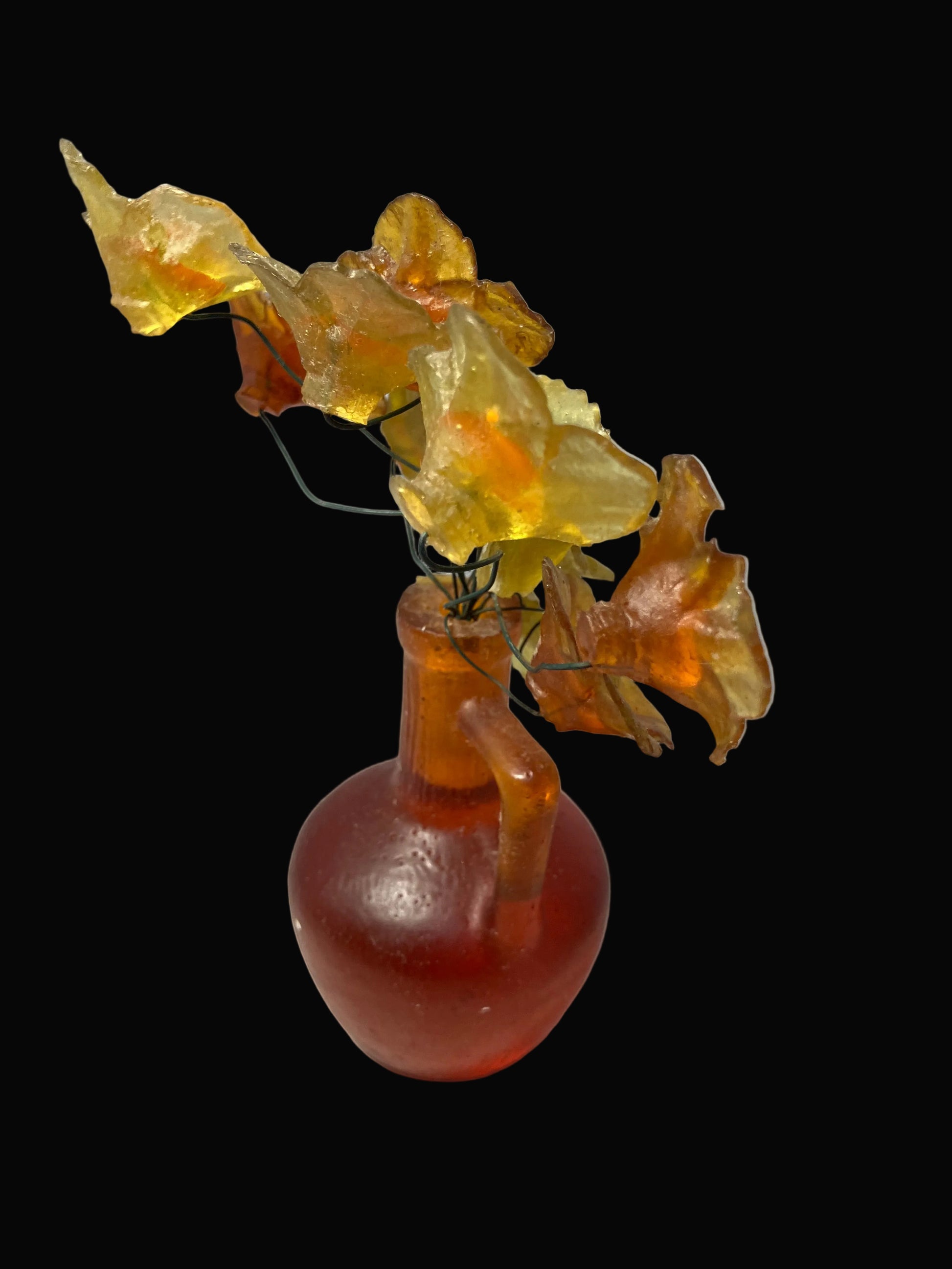 Artificial flower arrangement with yellow and orange flowers in a red glass vase on a black background