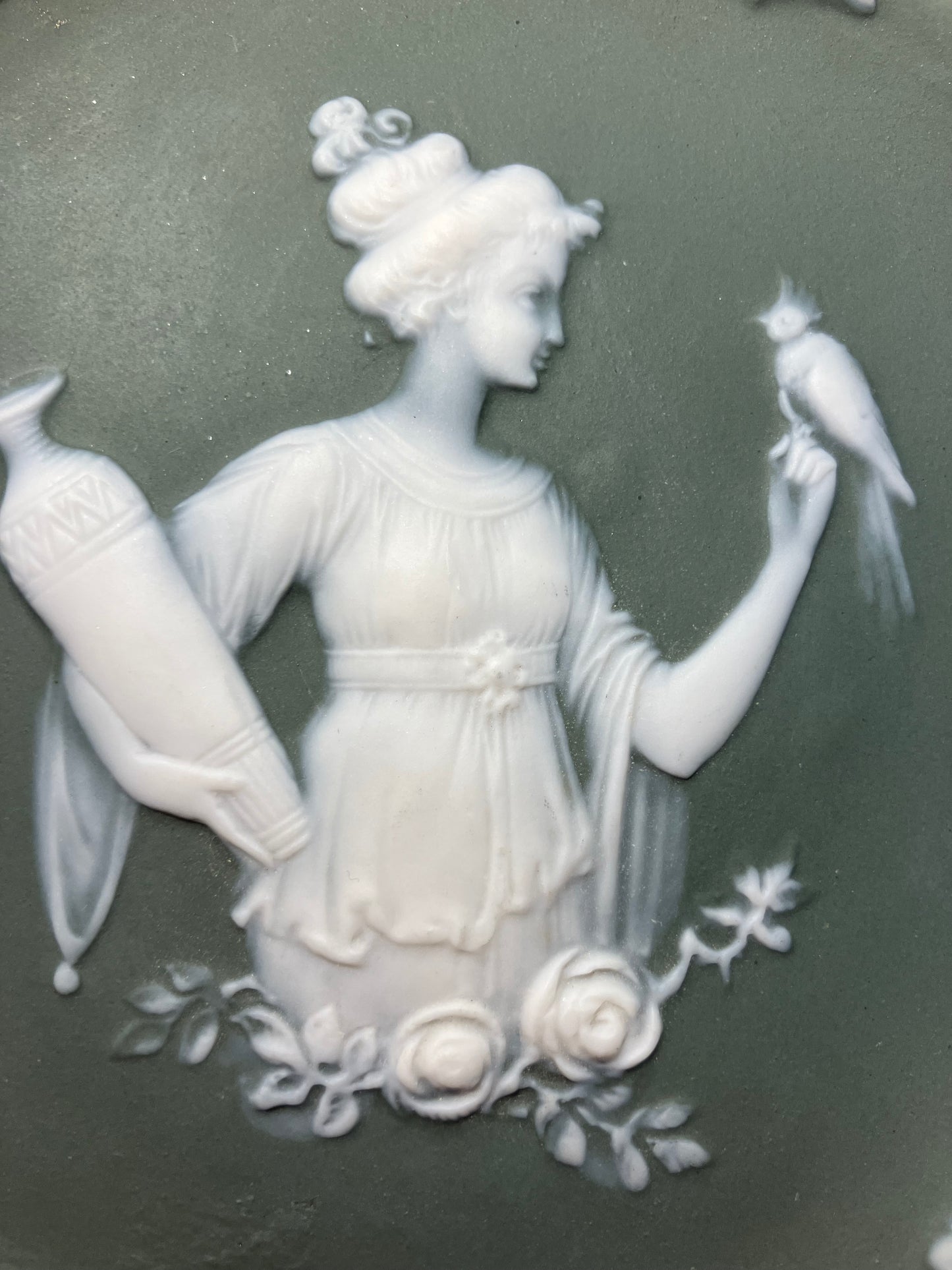 Decorative ceramic plate with a white relief of a woman and bird on a dark green background