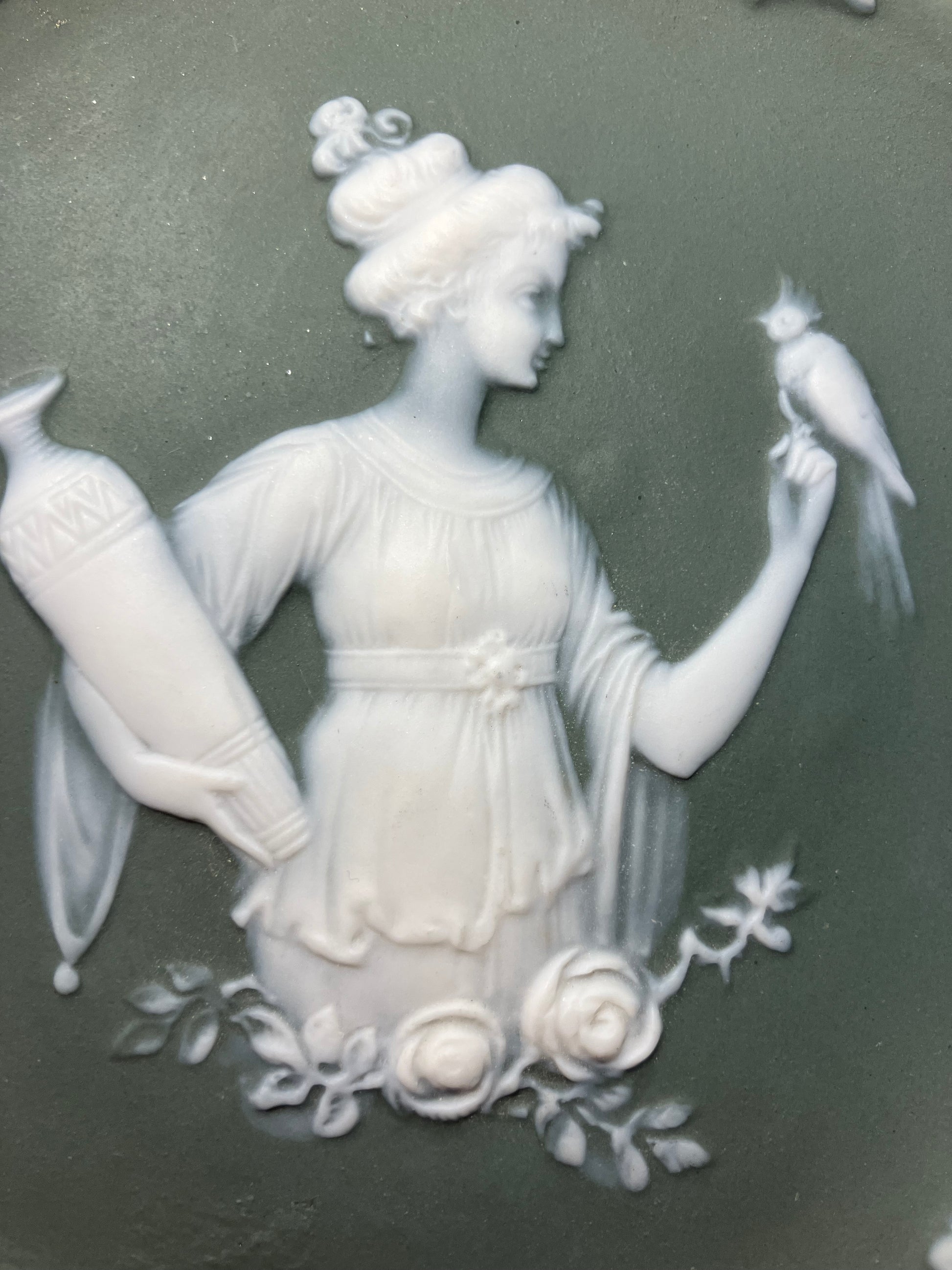 Decorative ceramic plate with a white relief of a woman and bird on a dark green background