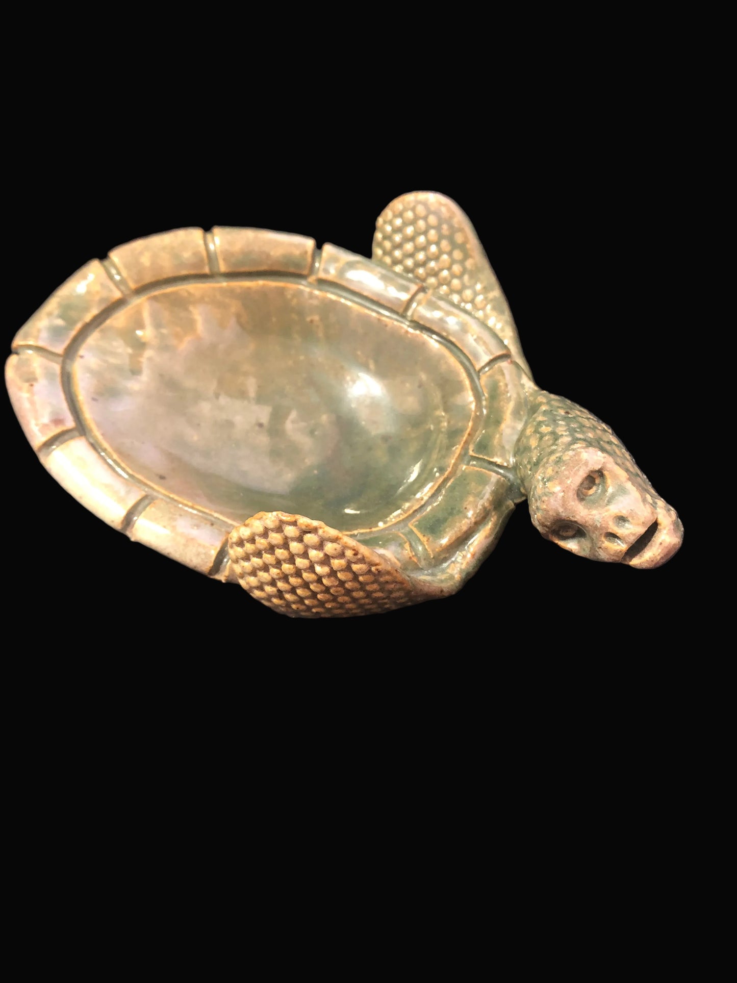 A pottery turtle-shaped bowl with a textured, basket-weave pattern on the shell and head, featuring a smooth, polished interior. The object is displayed on a dark background.