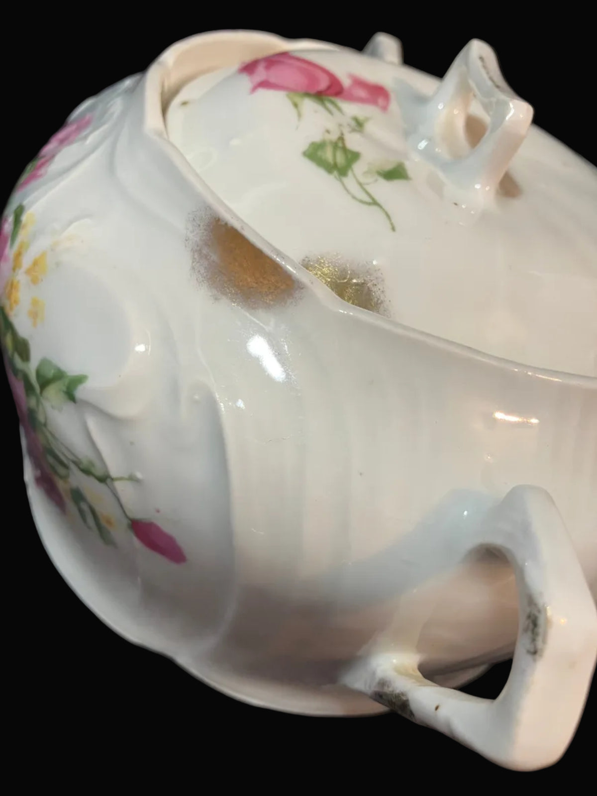 A close-up of a white porcelain sugar bowl with floral decoration, featuring pink roses and green leaves, with a small gold accent near the top.