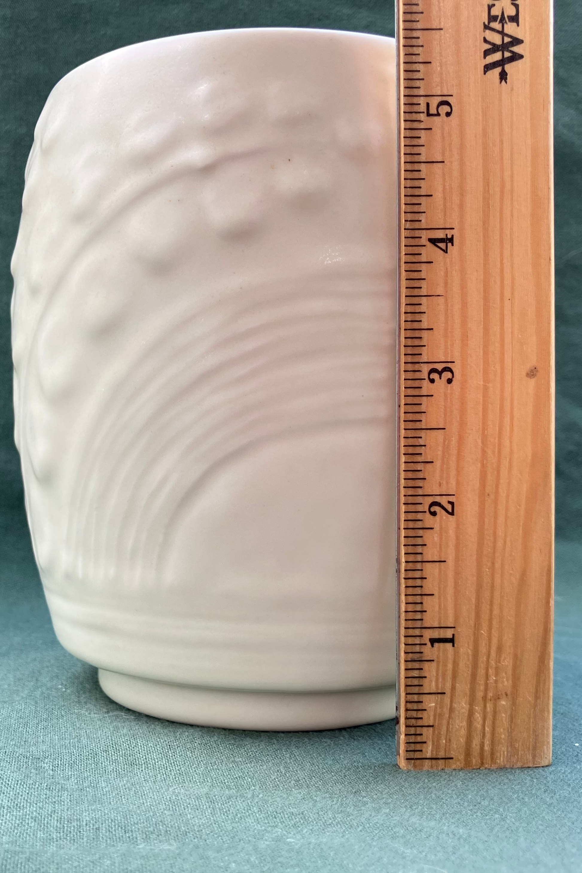 White textured vase next to a wooden ruler on a gray background