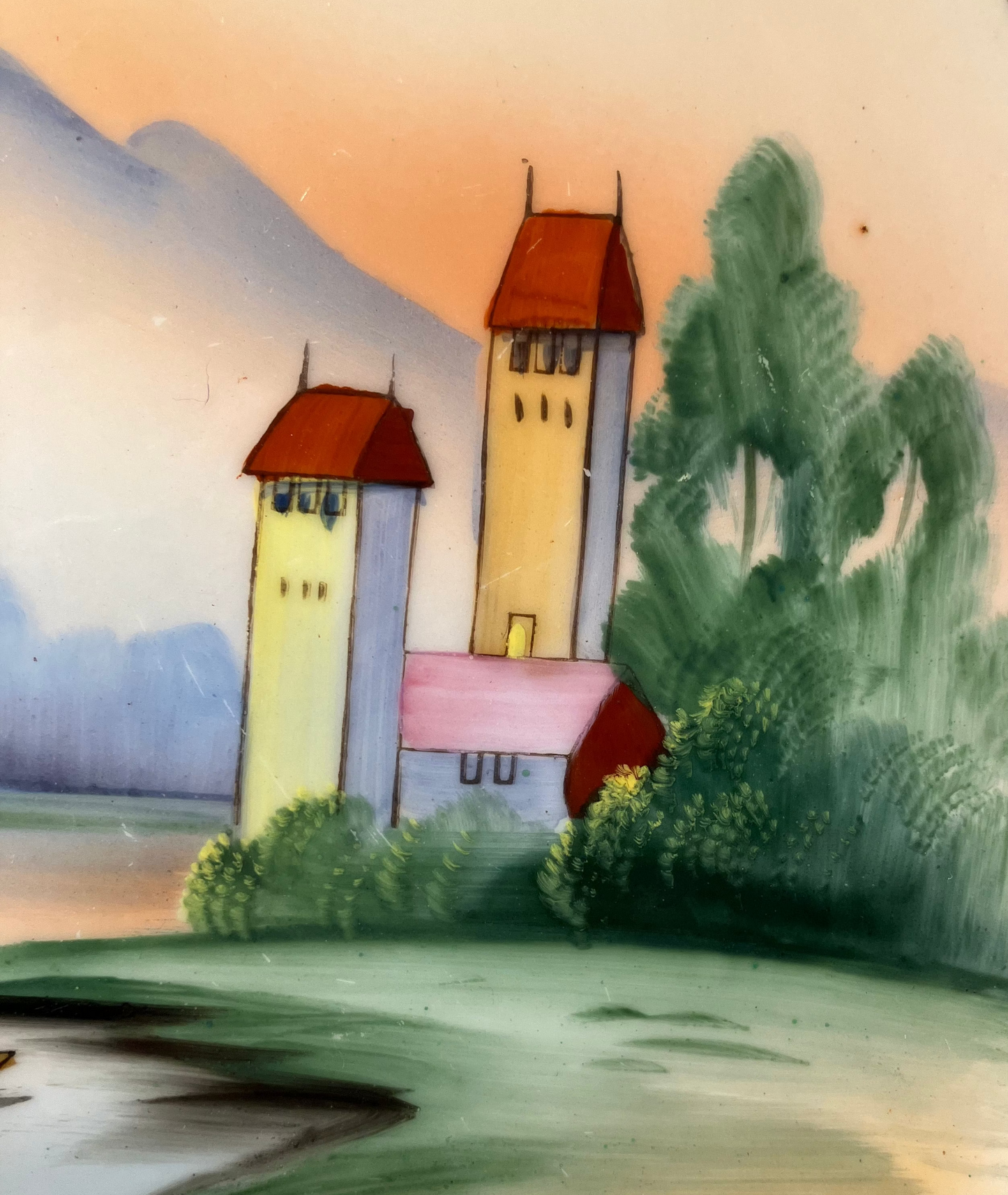 Painted scene of a village with houses and trees, framed by a green border.