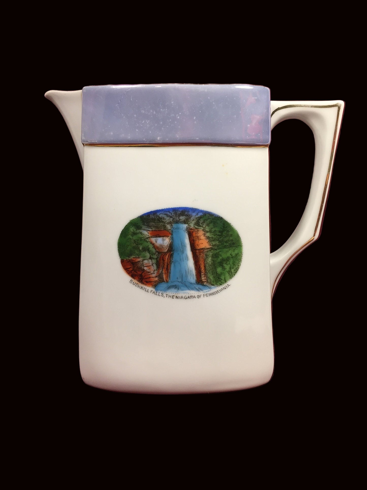 White ceramic pitcher with a blue rim and gold trim. The pitcher has a picture of a waterfall with the text &#39;Bushkill Falls, The Niagara of Pennsylvania&#39;.